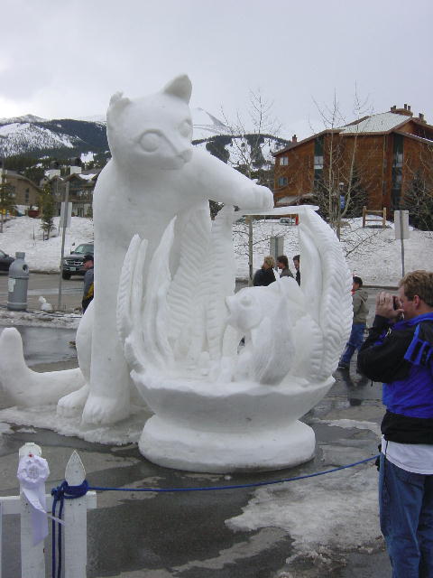 An ice sculpture of a cat reaching into a fish bowl.